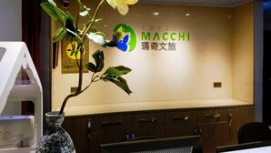 Een receptiebalie met een logo voor 'Hotel Macchi' en een decoratieve plant.