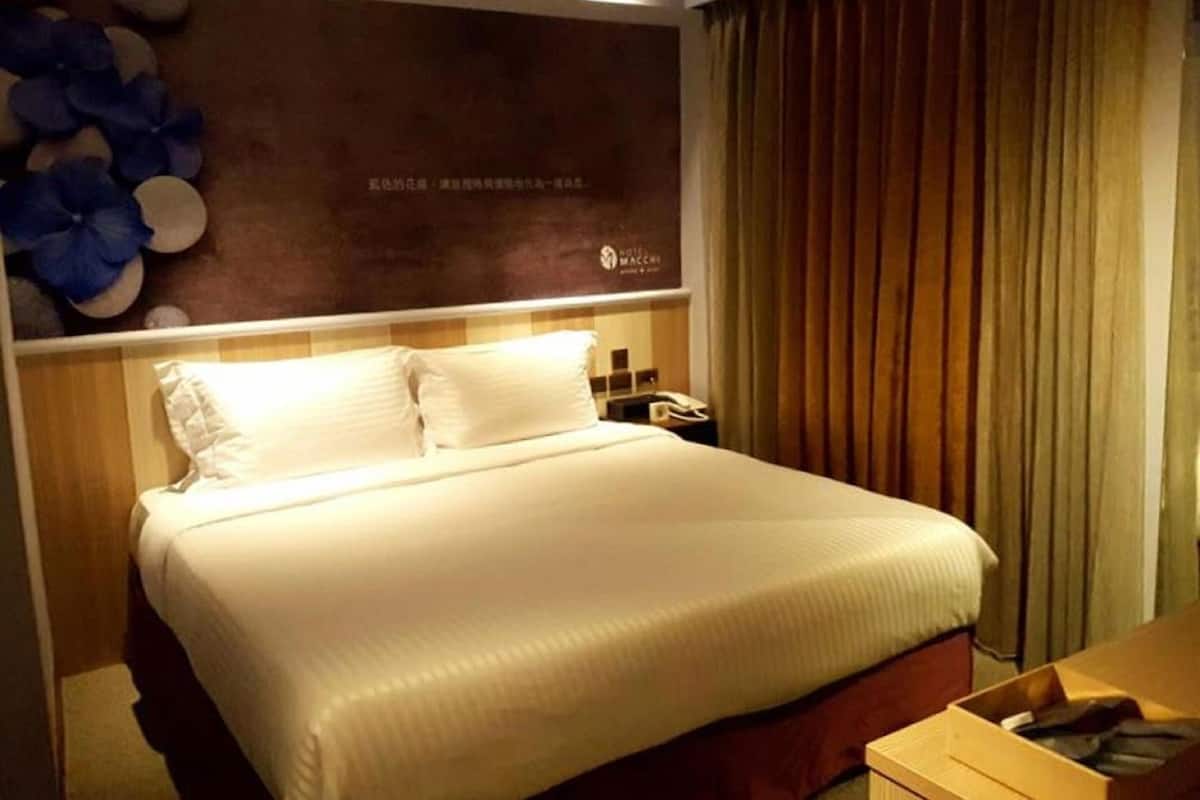 A hotel room with a bed, a nightstand, a telephone, and a wall with a floral design.