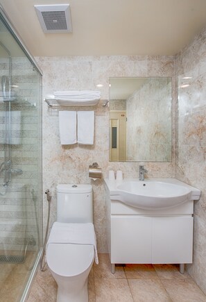 Un baño moderno con cabina de ducha de vidrio, inodoro blanco, lavamanos con espejo y toallero.