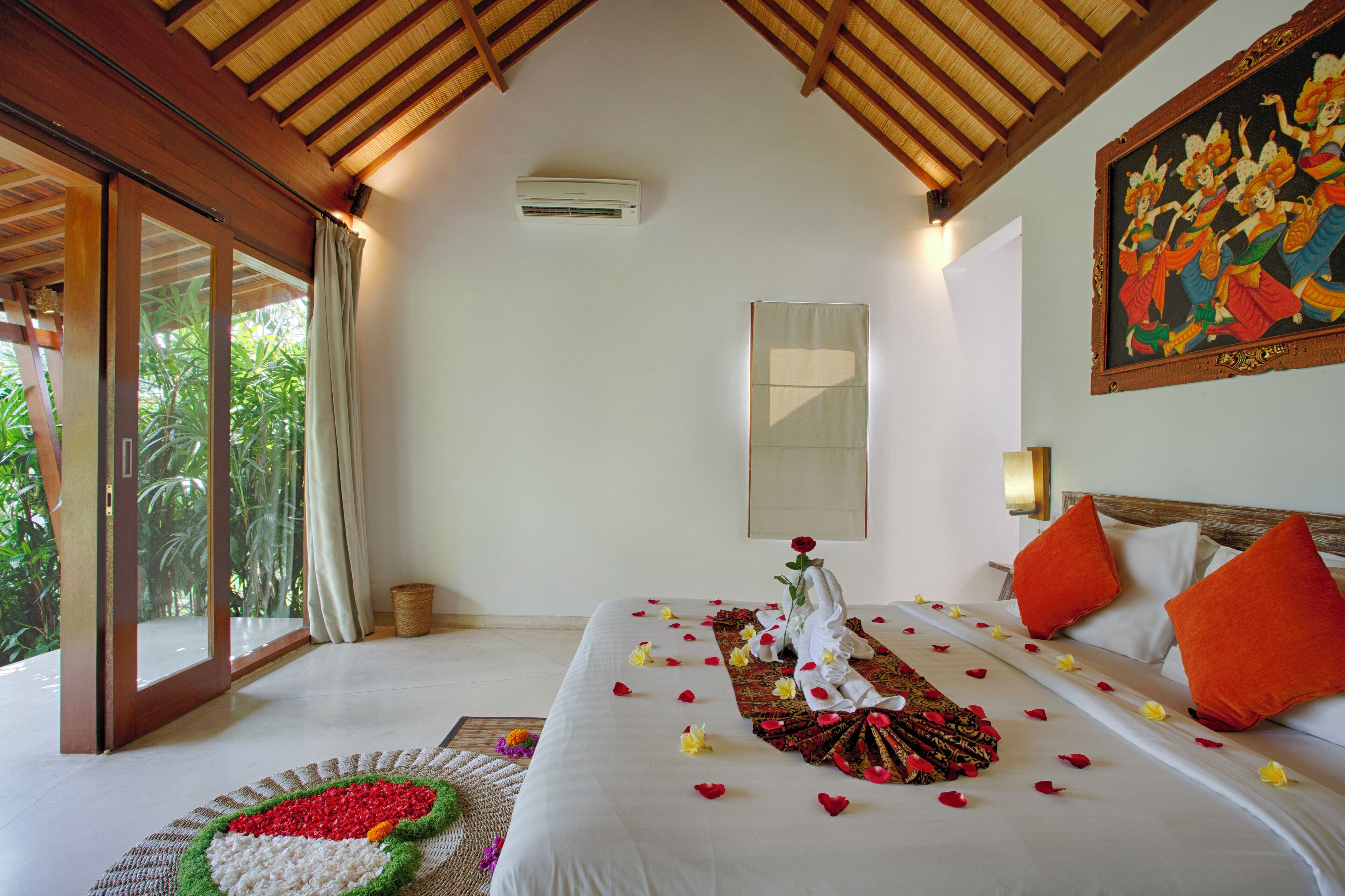 A hotel room with a large bed, a painting on the wall, and a view of greenery through the window.