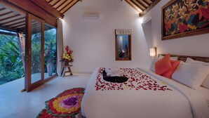 A bedroom with a bed, a painting, a window, and a door leading to a balcony. - Villa Tegal Tis Ubud (Ubud)