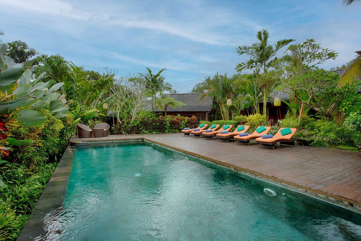 Piscina com espreguiçadeiras e plantas tropicais.