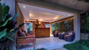 A modern reception area with a wooden reception desk, comfortable seating, and large windows offering a view of the outdoors. - Villa Tegal Tis Ubud (Ubud)