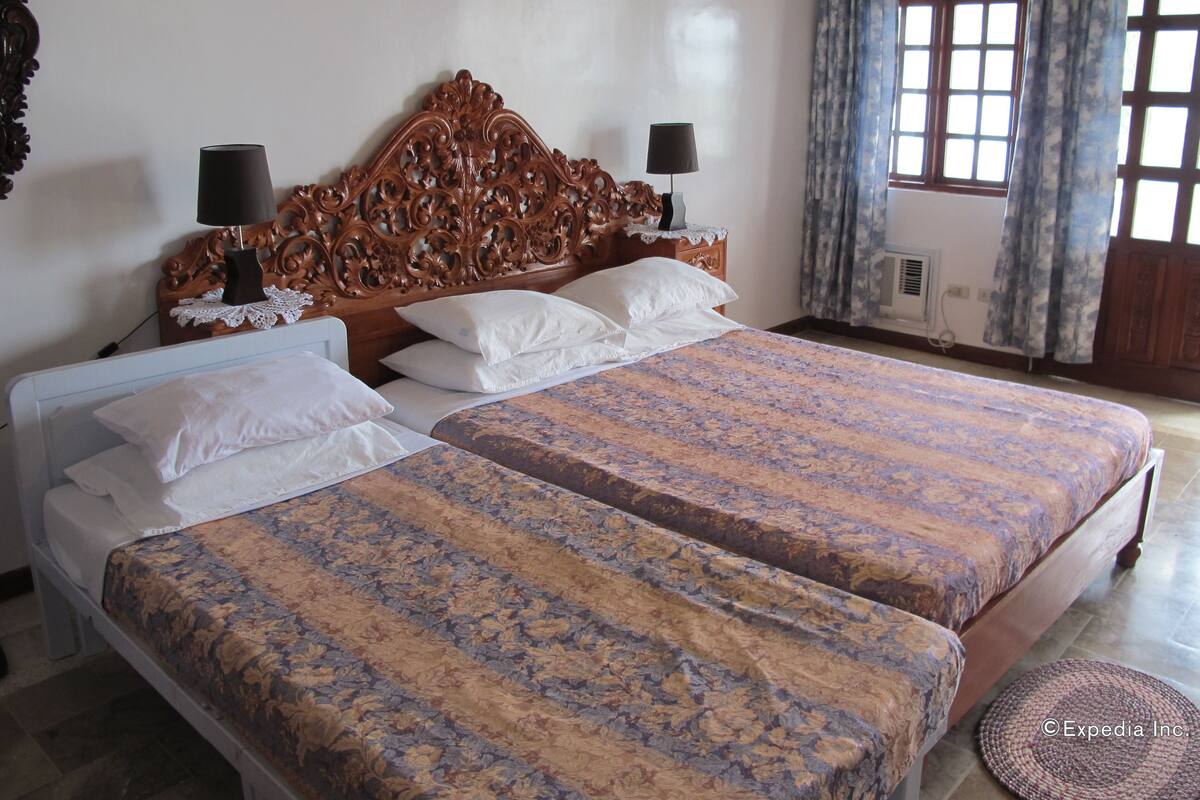 Un lit double avec une couvre-lit à motifs floraux, une tête de lit en bois et deux lampes de chevet.
