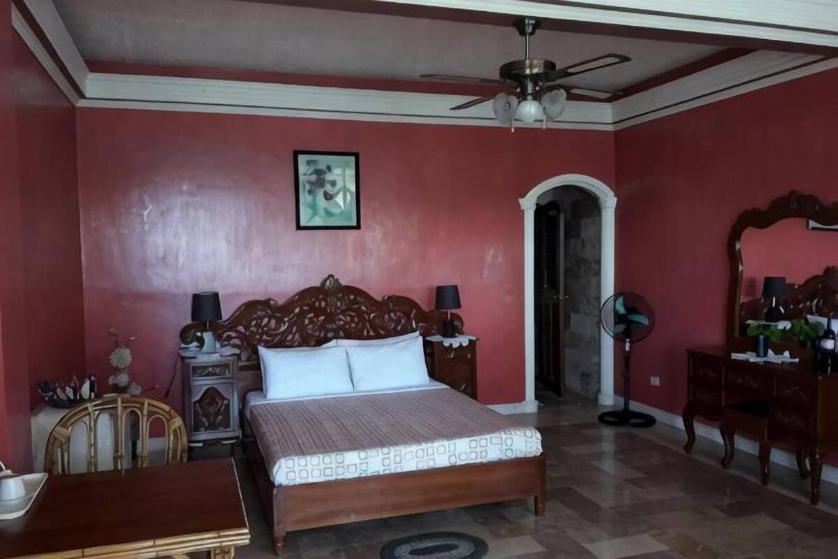 Une chambre à coucher comprenant un lit, un ventilateur de plafond, un bureau, une chaise, une commode et un miroir.