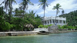 Un bâtiment de style colonial, peint en blanc, avec un toit de chaume et une clôture blanche.