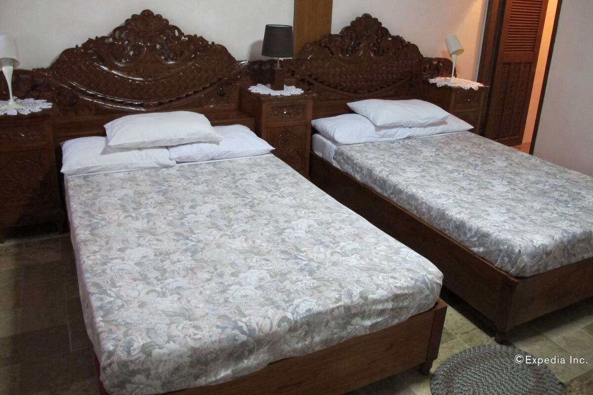 Un lit double avec une couvre-lit à motifs floraux, une tête de lit en bois, des tables de chevet avec des lampes et une armoire en bois.