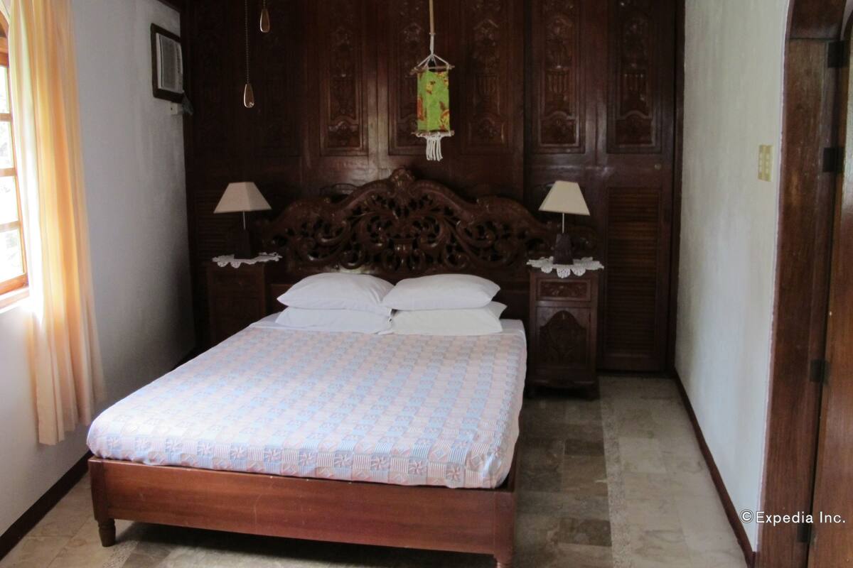 Une chambre à coucher avec un lit en bois, deux tables de chevet avec des lampes, un luminaire suspendu et une armoire en bois.