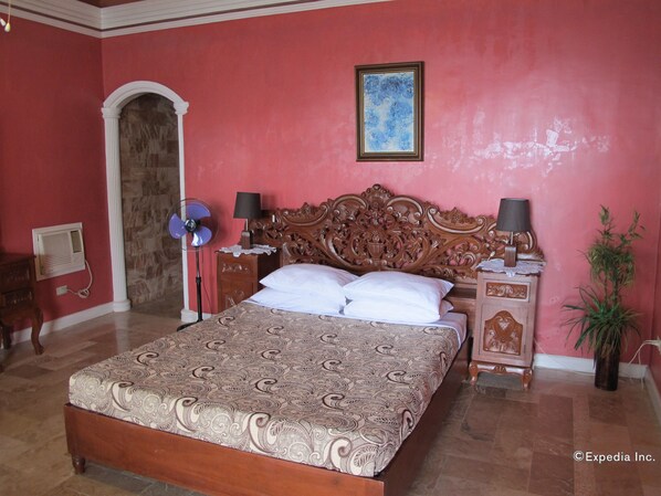 Un dormitorio con una cama grande, cabecera de madera, mesita de noche, lámpara y una planta en maceta.