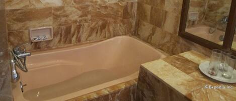 A bathroom with a marble wall, a bathtub, a sink, and a mirror.