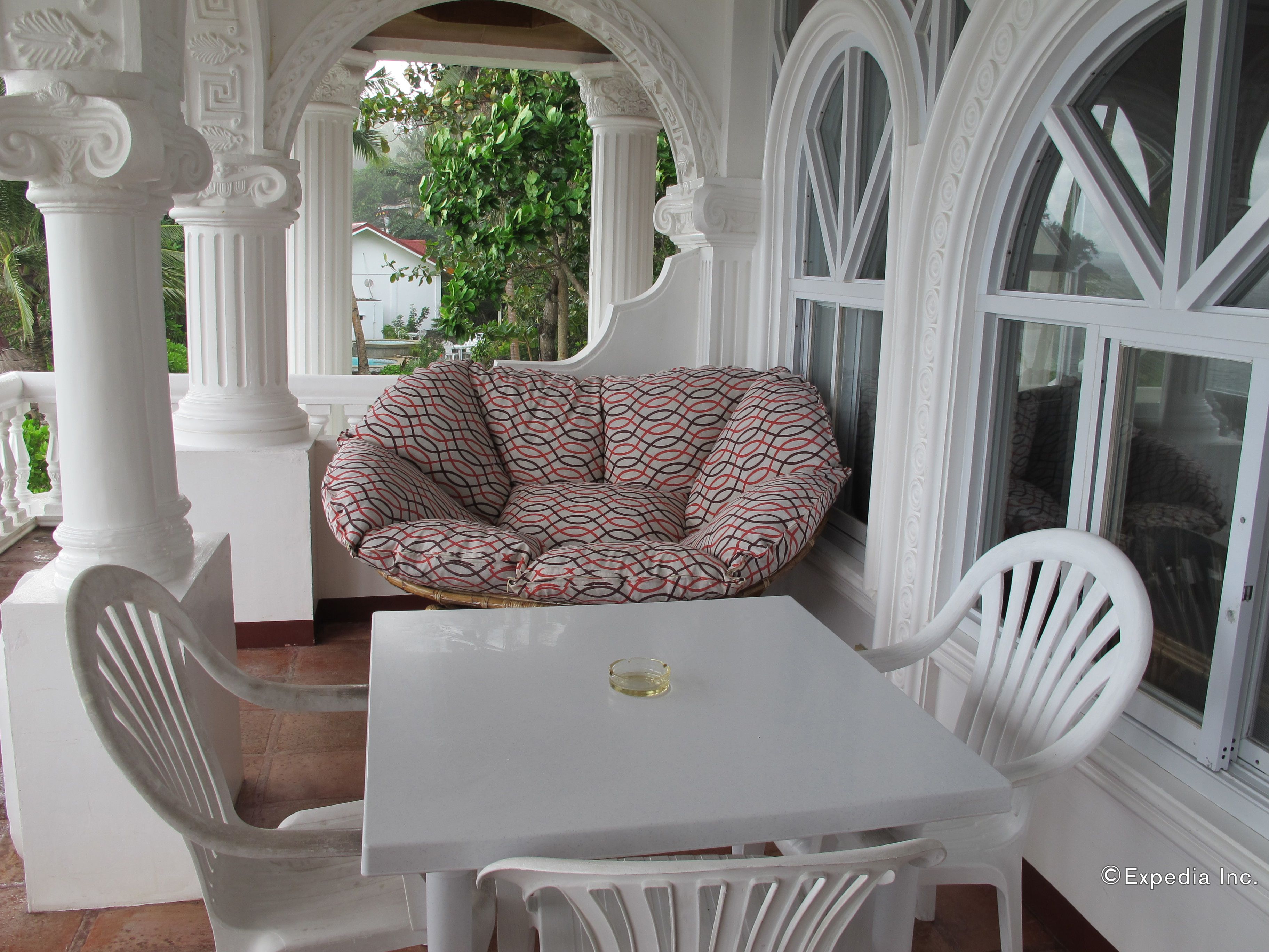 Une table et des chaises blanches, disposées dans un espace extérieur abrité, avec un fauteuil en forme de sac de haricots à motifs.