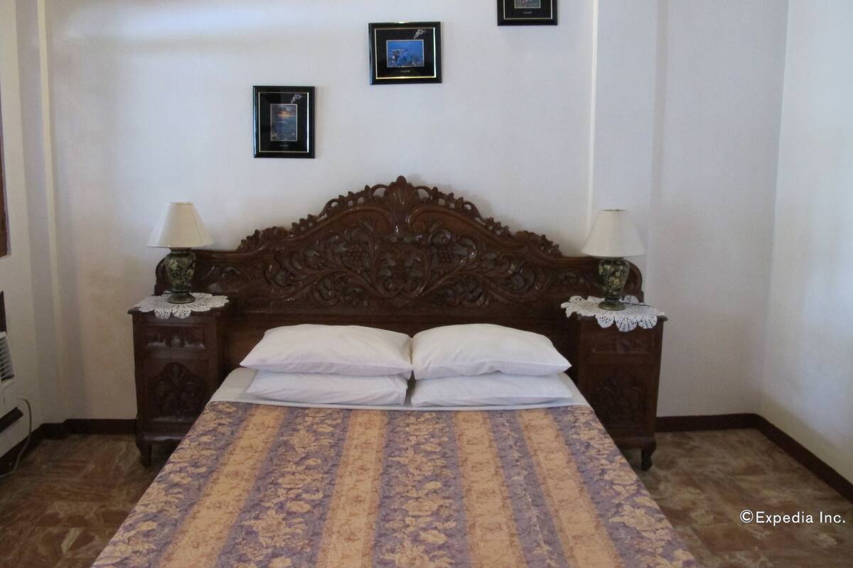 Une chambre à coucher avec une tête de lit en bois, deux tables de chevet avec des lampes et une couvre-lit à motifs.