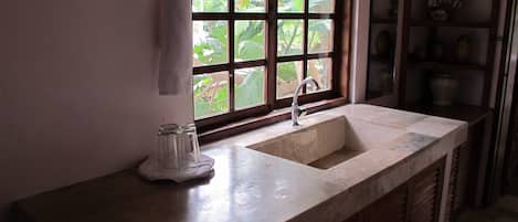 A kitchen with a marble countertop, a sink, a window with a view of greenery, and wooden cabinets.