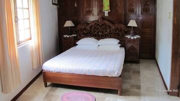 Quarto com cama de madeira, duas mesas de cabeceira com luminárias, uma janela com cortinas e um lustre.