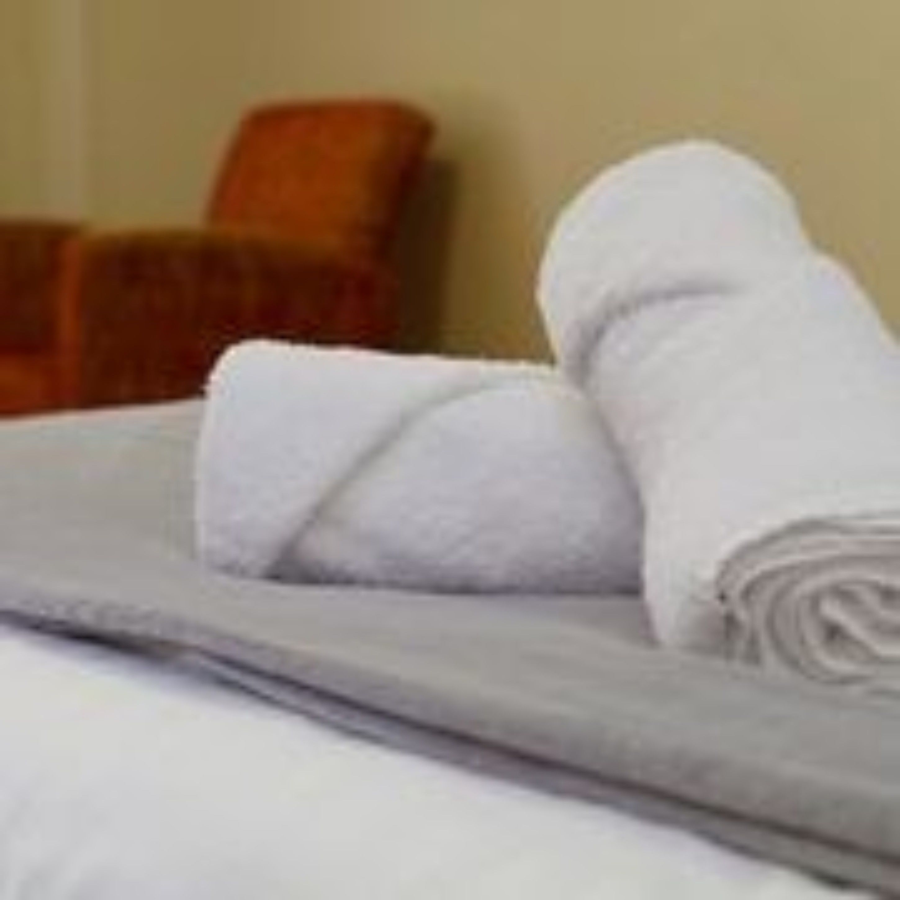 Una cama bien tendida con sábanas blancas y una toalla blanca doblada.
