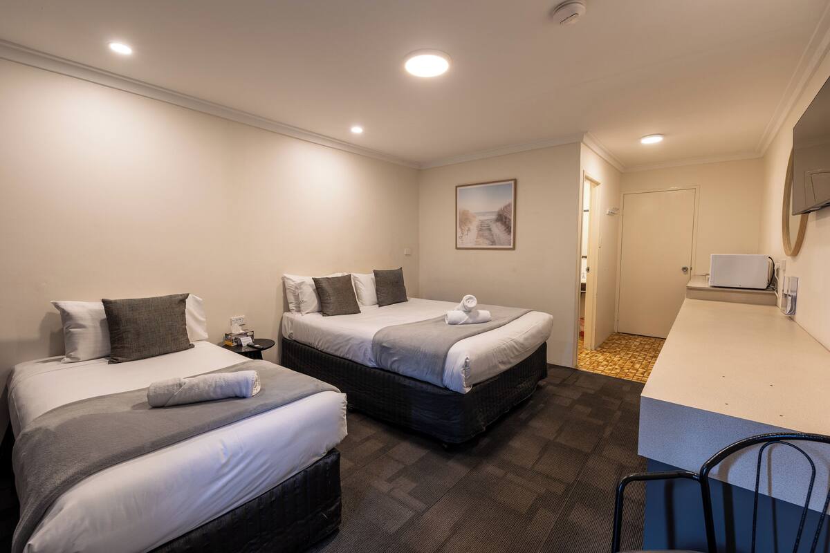 A hotel room with two beds, a small desk, a chair, a mirror, and a door leading to a bathroom.