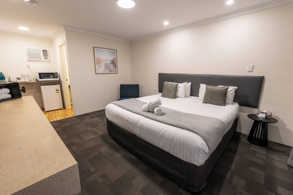 A hotel room with a bed, a small desk, a microwave, a refrigerator, and a picture on the wall.