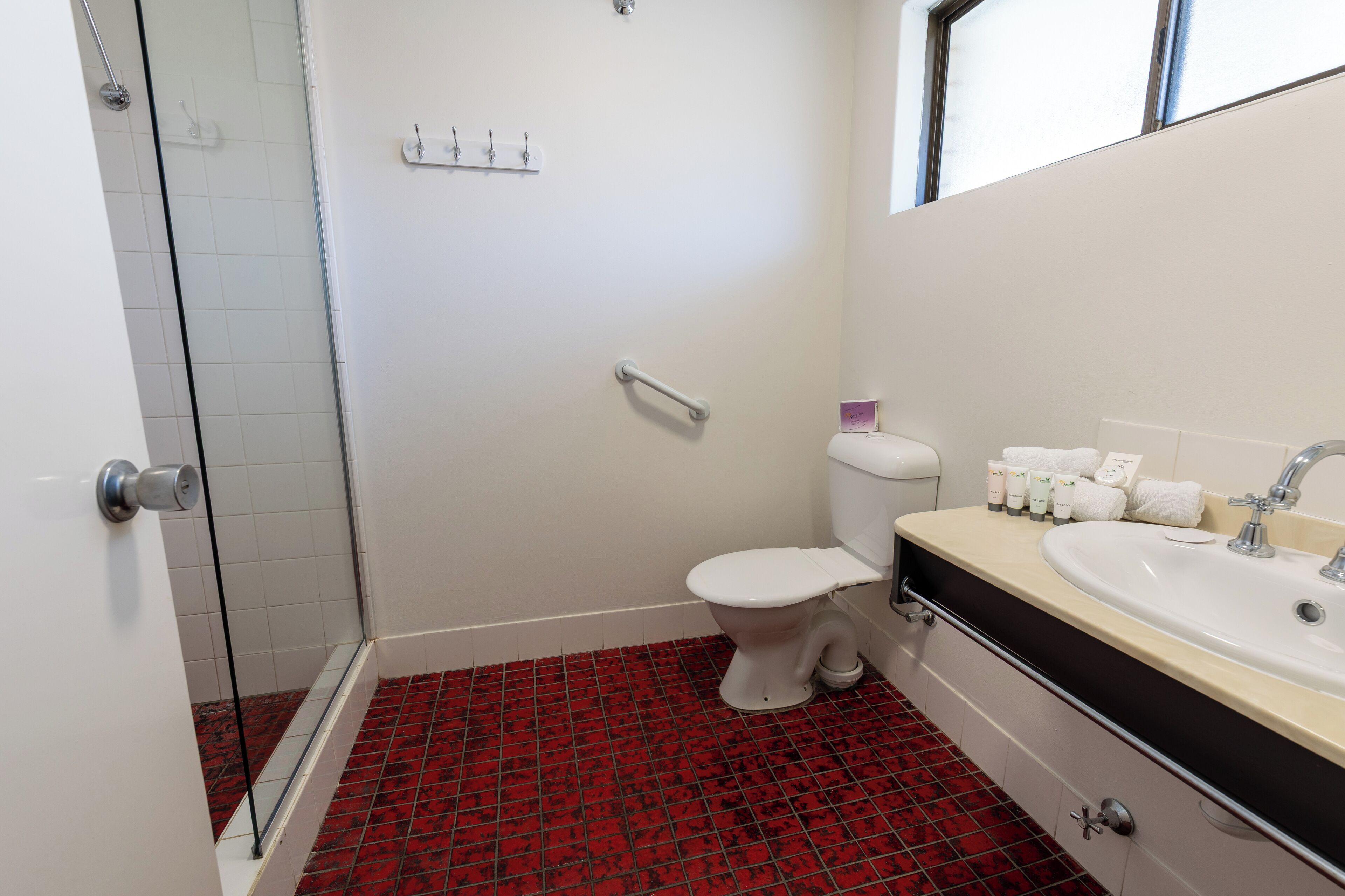 A bathroom with a shower, toilet, sink, and a red-tiled floor.