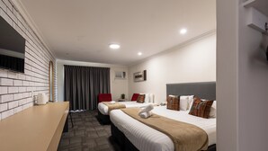 Ein Hotelzimmer mit zwei Betten, einem Flachbildfernseher, einem Schreibtisch und einem Fenster mit Vorhängen.