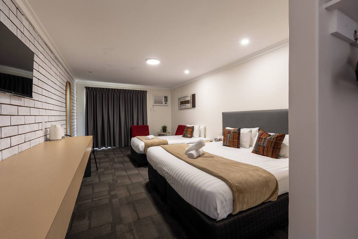 A hotel room with two beds, a flat-screen TV, a desk, and a window with curtains.