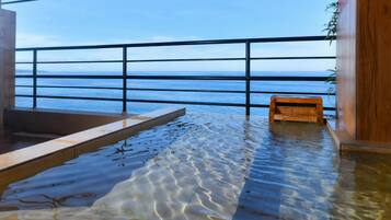 An indoor pool with clear water, a wooden bench, and a view of the sea through a metal railing.