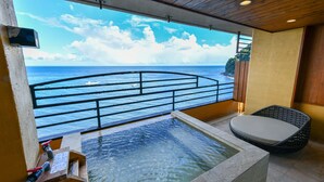 A balcony with a view of the sea, a small pool, and a wicker chair.