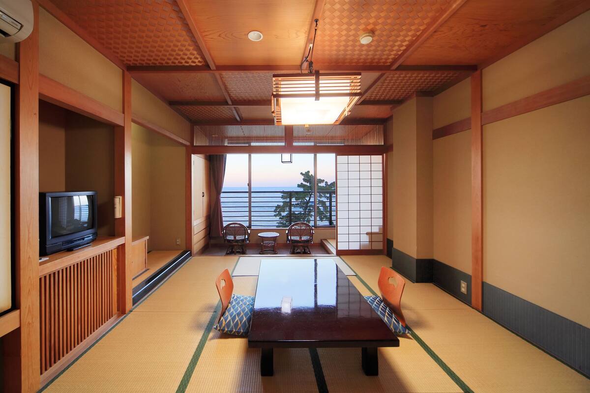 Une pièce de style japonais traditionnel, avec un sol recouvert de tatamis, une table basse et un téléviseur posé sur une étagère.