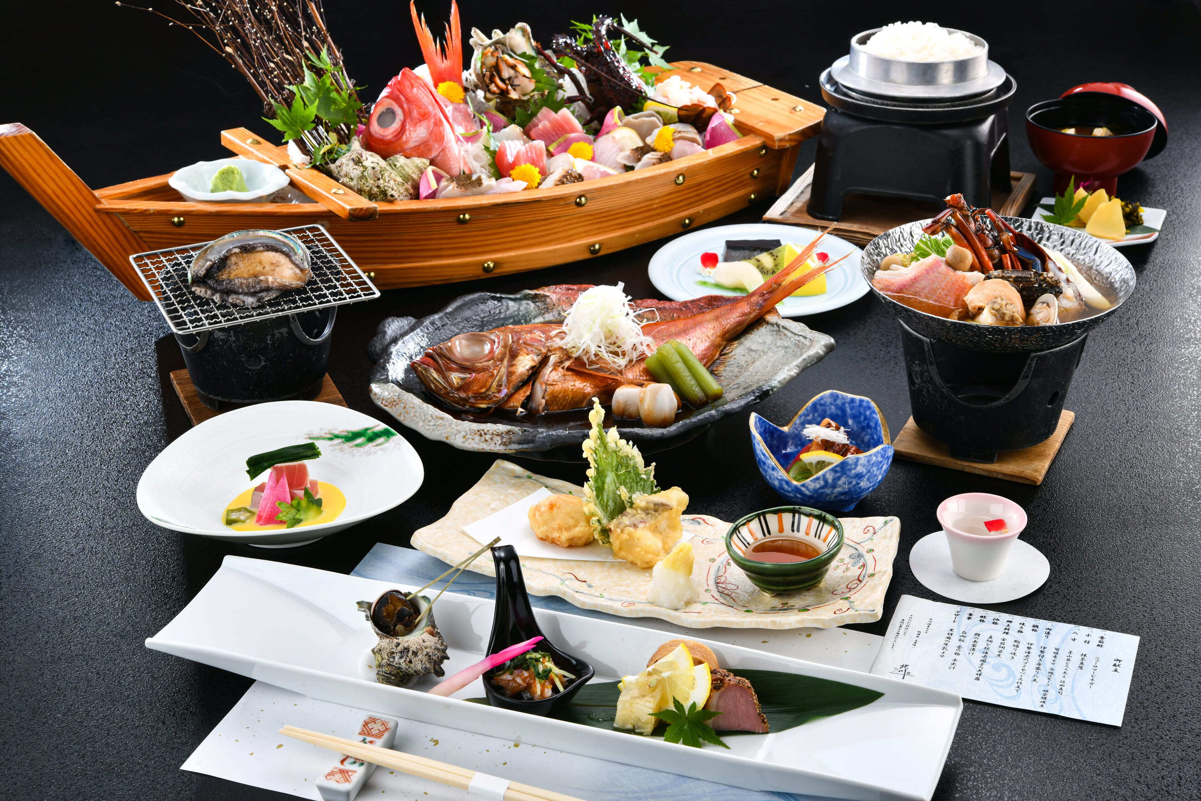 A variety of dishes including seafood, vegetables, and rice, arranged on a table with a menu and chopsticks.