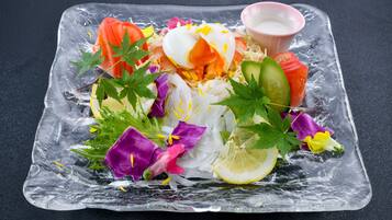 A clear glass dish with a salad, including sliced vegetables and a poached egg, on a dark surface.