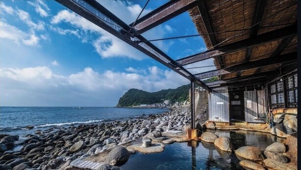 A stone pathway leading to a wooden structure by the sea, with clear water and a view of the ocean.