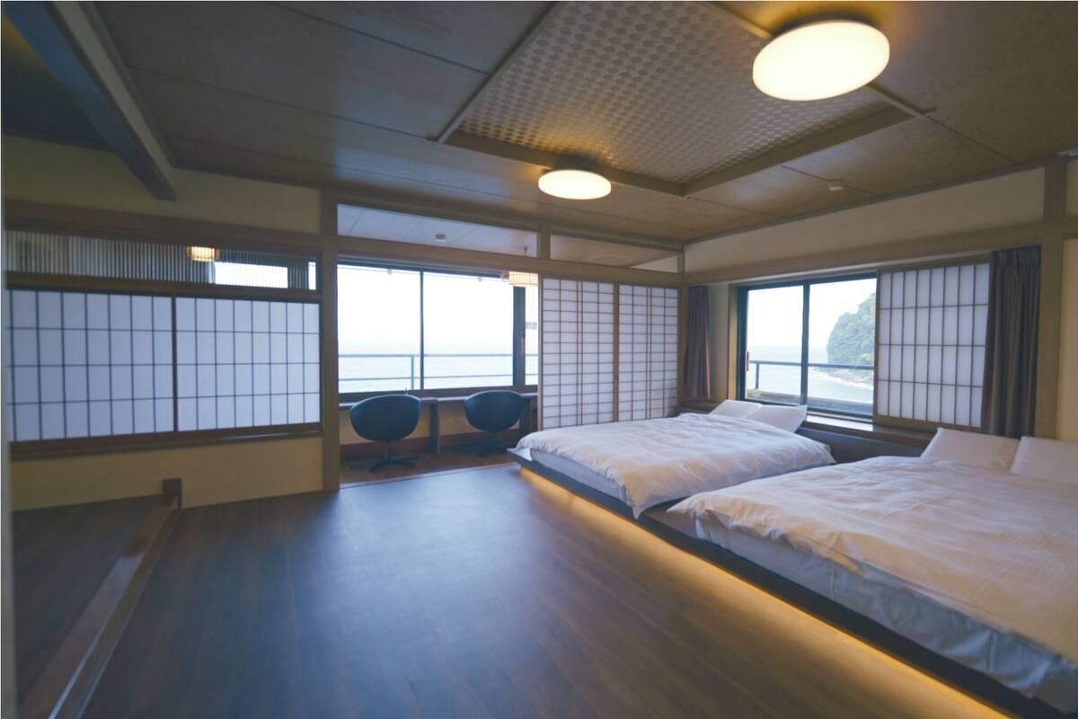Une pièce de style japonais traditionnel, avec un sol recouvert de tatamis, deux lits, des paravents shoji et une vue sur la mer.