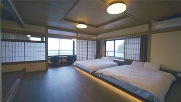 A traditional Japanese-style room with tatami flooring, two beds, shoji screens, and a view of the sea.