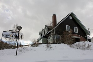 A large house with a chimney, a signboard, and a snow-covered ground.