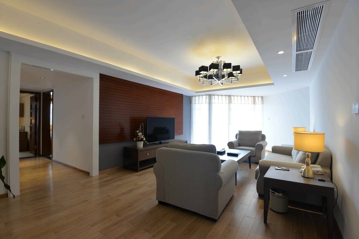 Een moderne woonkamer met een flatscreen televisie, banken, een salontafel en een lamp.