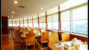 A spacious dining area with wooden tables and chairs, large windows offering a view of the cityscape, and a sign indicating a smoking area.