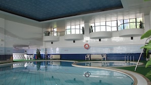 An indoor swimming pool with multiple lanes, a lifeguard stand, and a seating area with chairs.