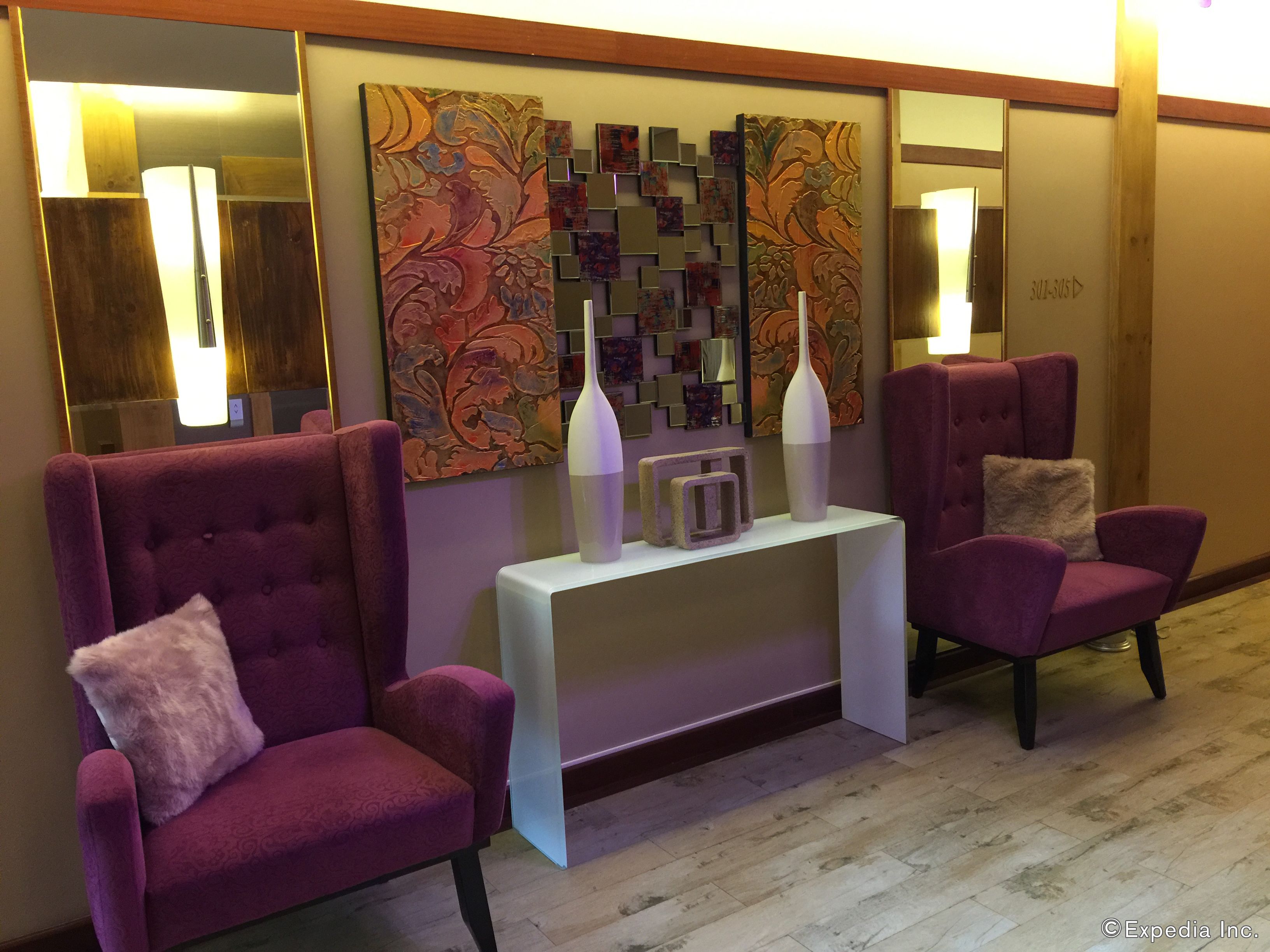 A lobby with two purple armchairs, a white console table with two vases, and a wall with abstract art.
