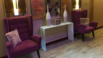 A lobby with two purple armchairs, a white console table with two vases, and a wall with abstract art.