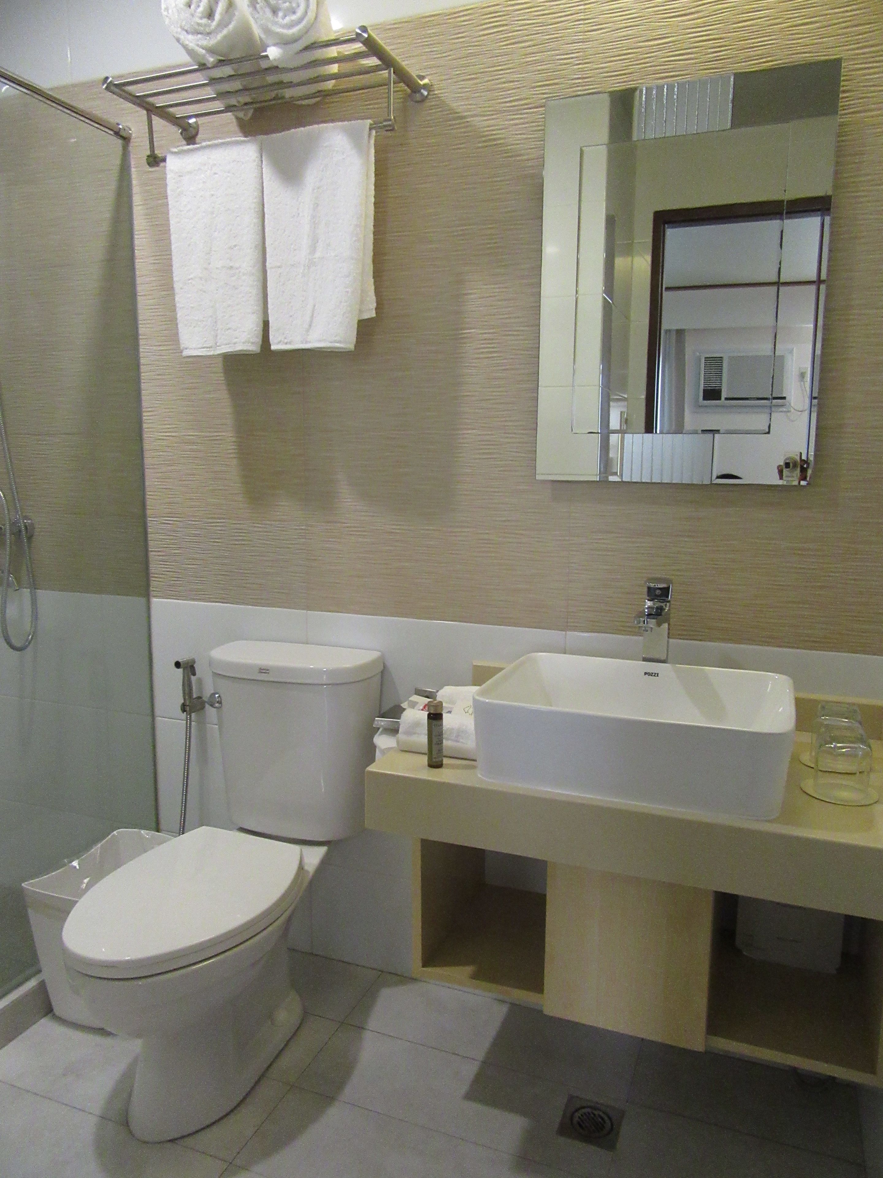 A bathroom with a toilet, sink, and shower. There are towels hanging on a rack and a mirror above the sink.