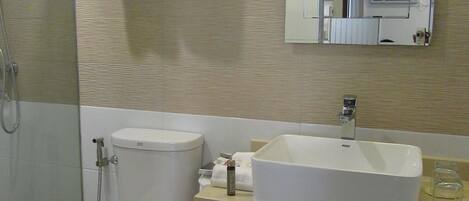 A bathroom with a toilet, sink, and shower. There are towels hanging on a rack and a mirror above the sink.