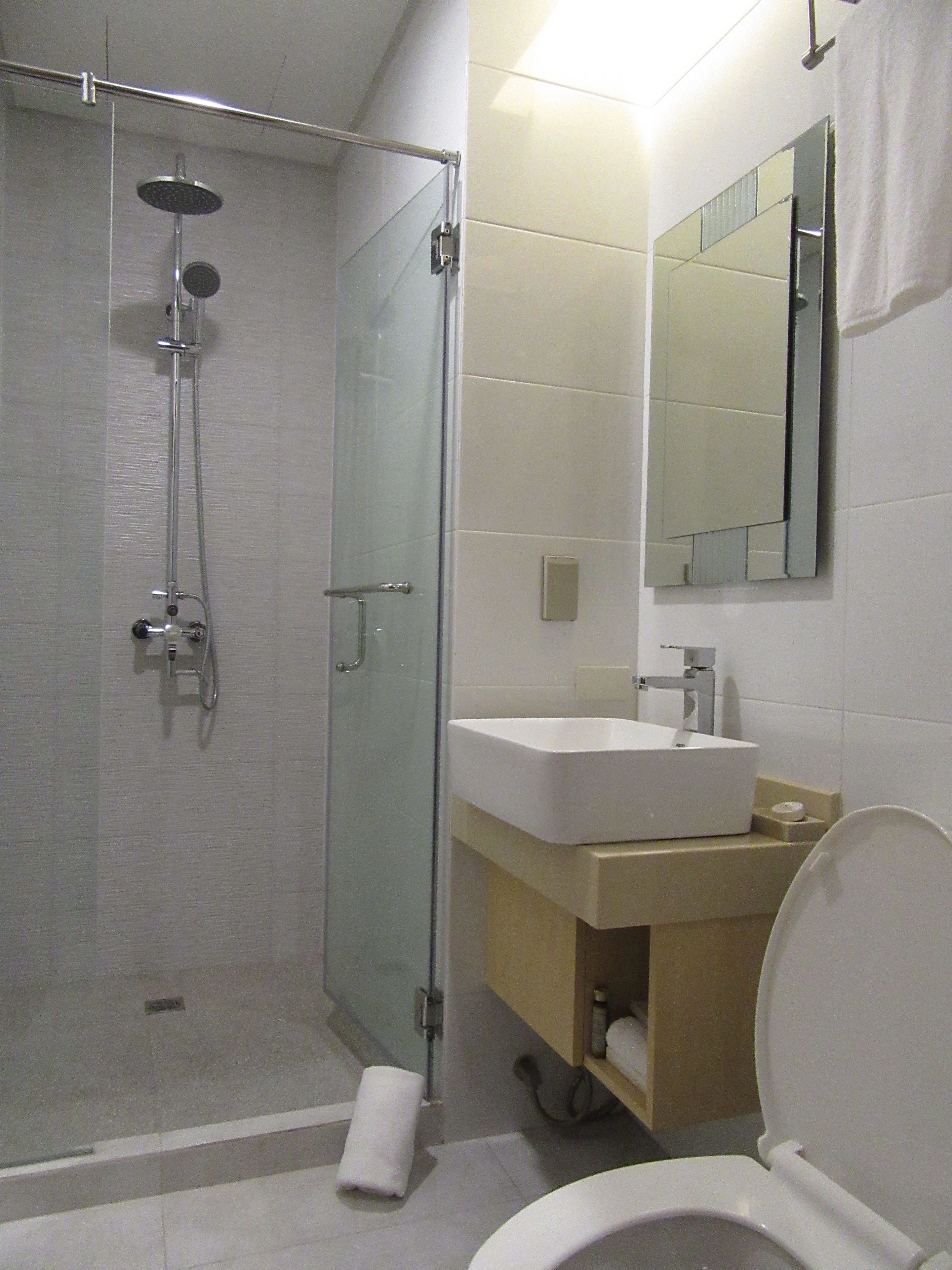 Een moderne badkamer met een douchecabine van glas, een witte wastafel en een toilet.