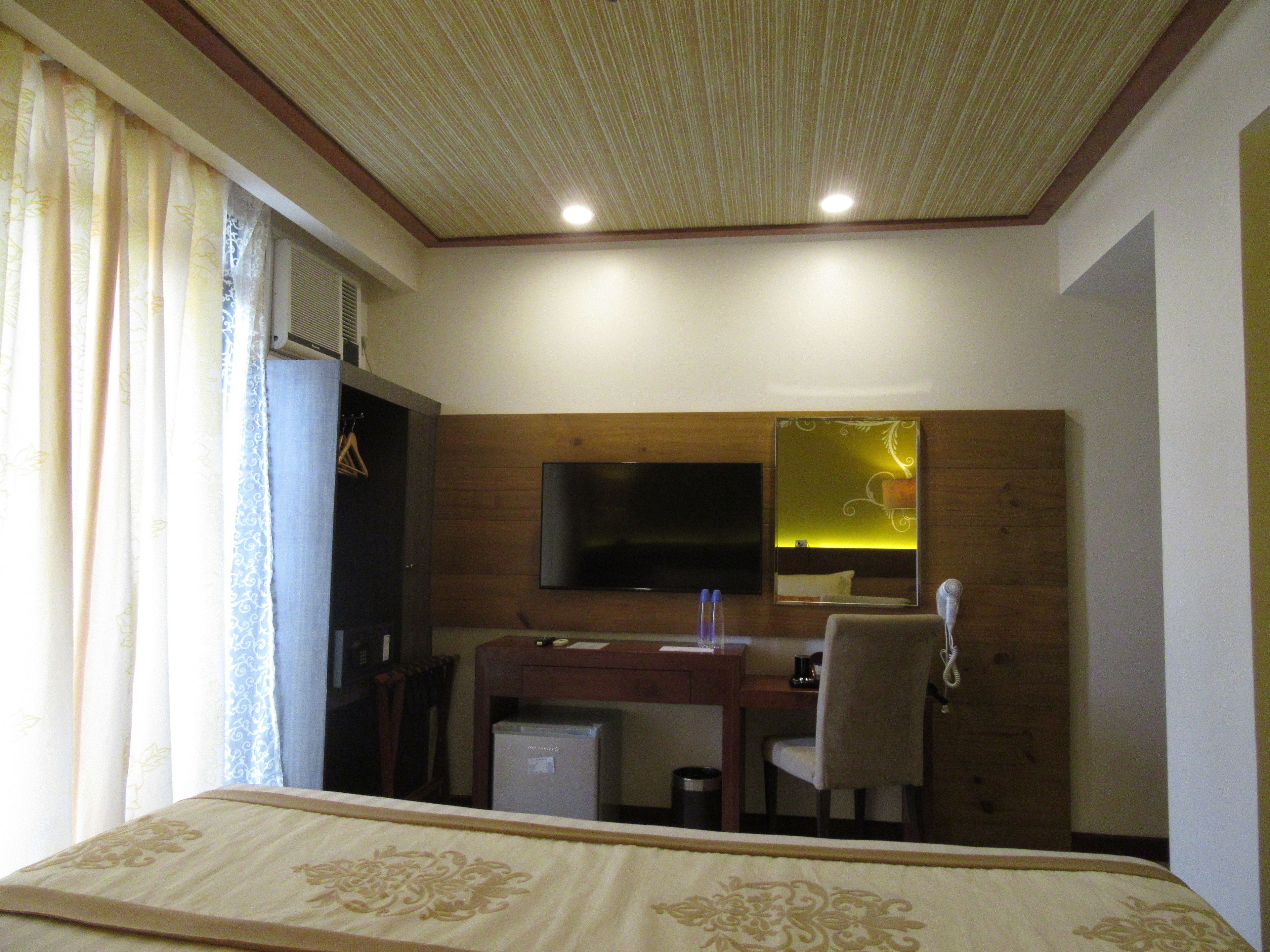 A hotel room with a bed, a desk, a chair, a television, and a small refrigerator.
