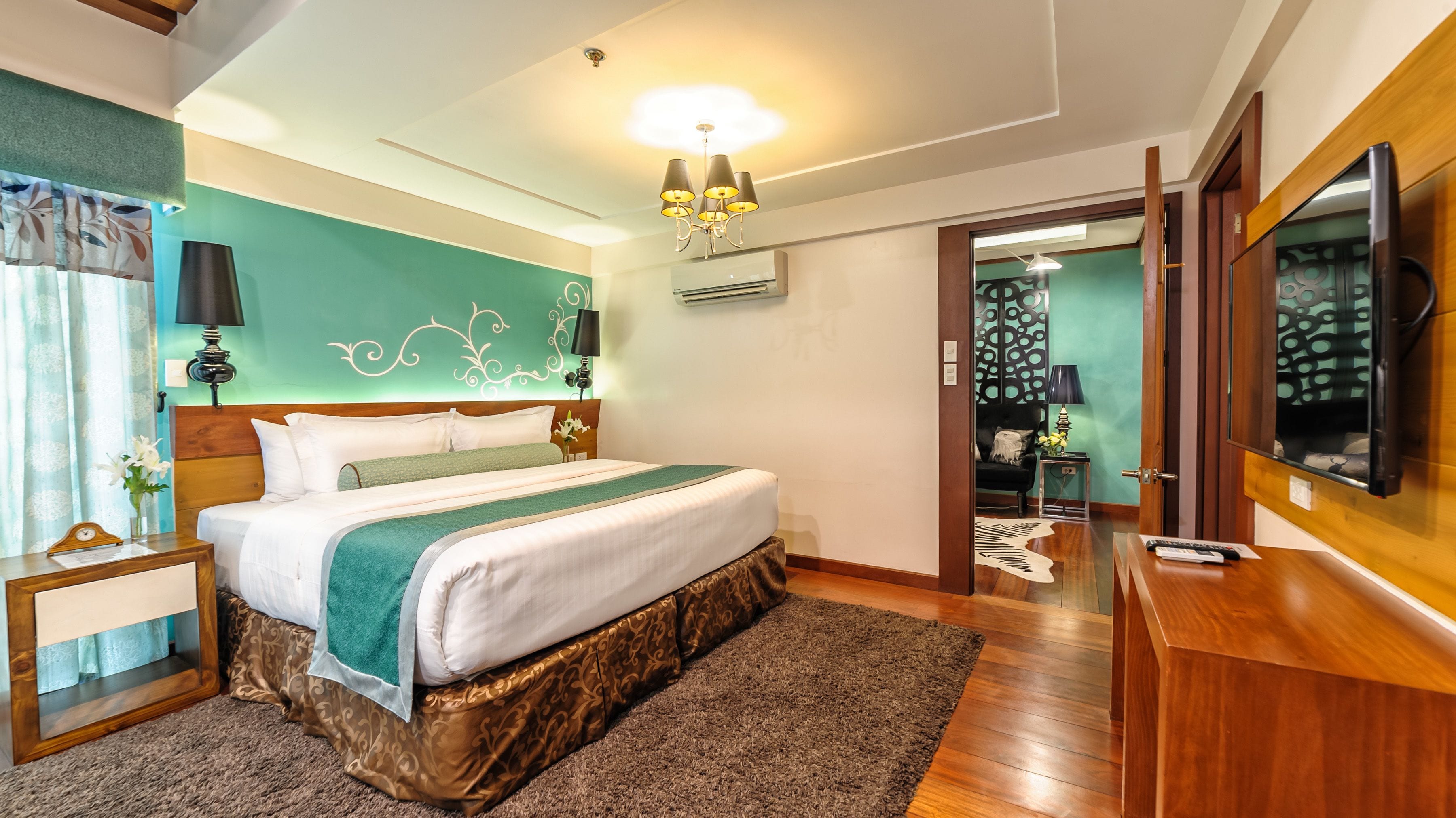 A modern hotel room with a large bed, a wooden nightstand, a desk, and a television.