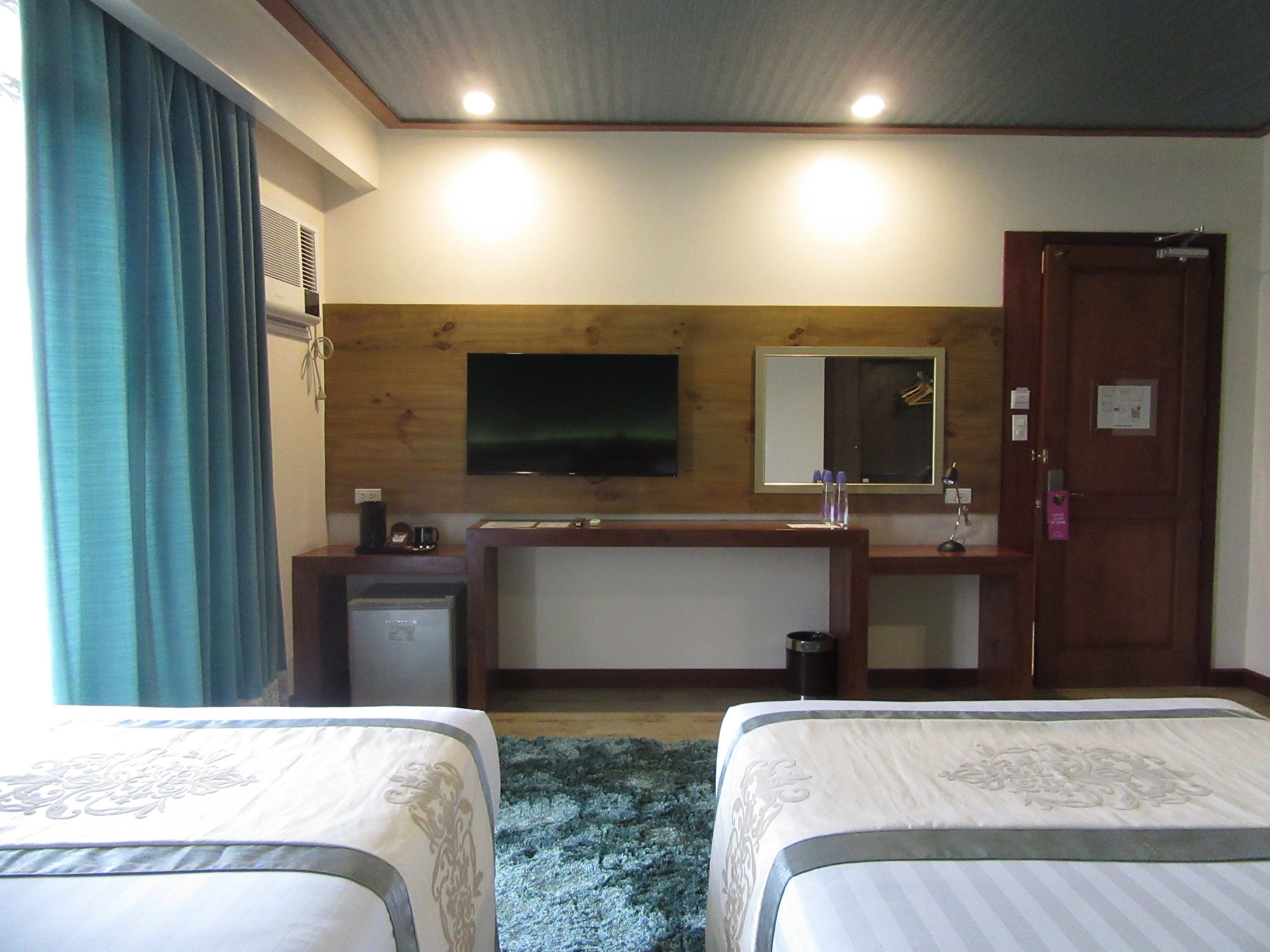 Ein Hotelzimmer mit zwei Betten, einem Schreibtisch, einem Spiegel, einem Fernseher und einer Tür.