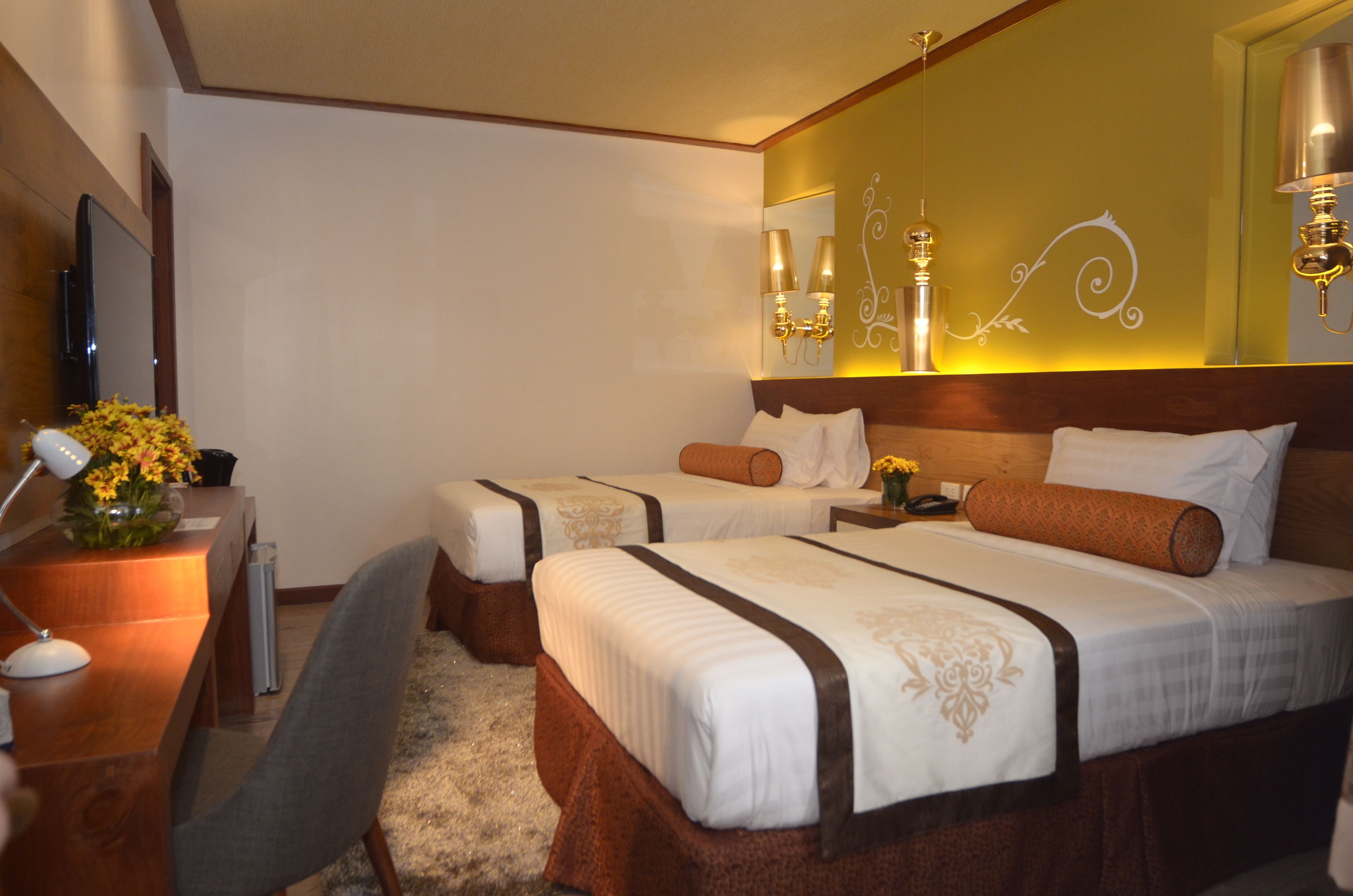 A hotel room with two beds, a desk, a chair, and a TV.