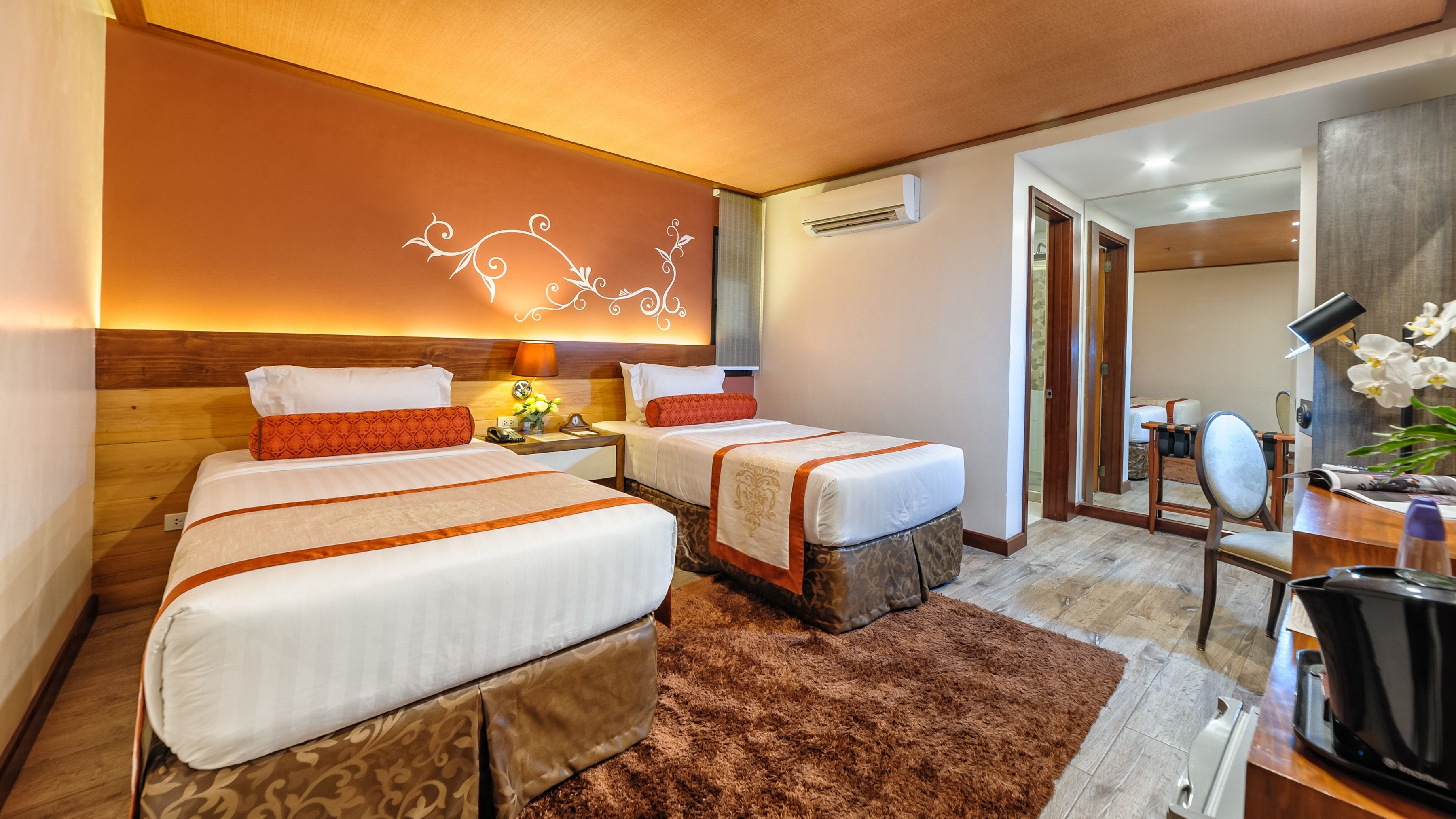 A hotel room with two beds, a desk, a chair, and a bathroom visible through an open door.