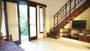 A hotel room with a bed, a TV, a staircase, and a sliding glass door leading to a balcony. - Praschita Bali (Denpasar)