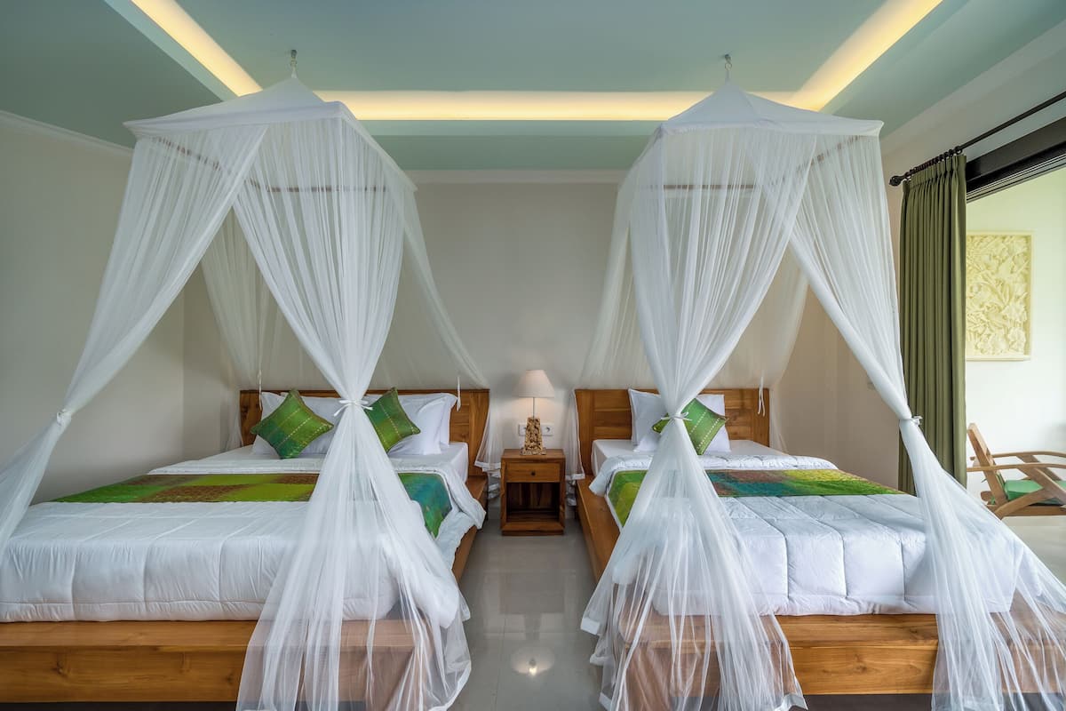 A hotel room with two beds, each with a canopy, wooden headboards, and green pillows.