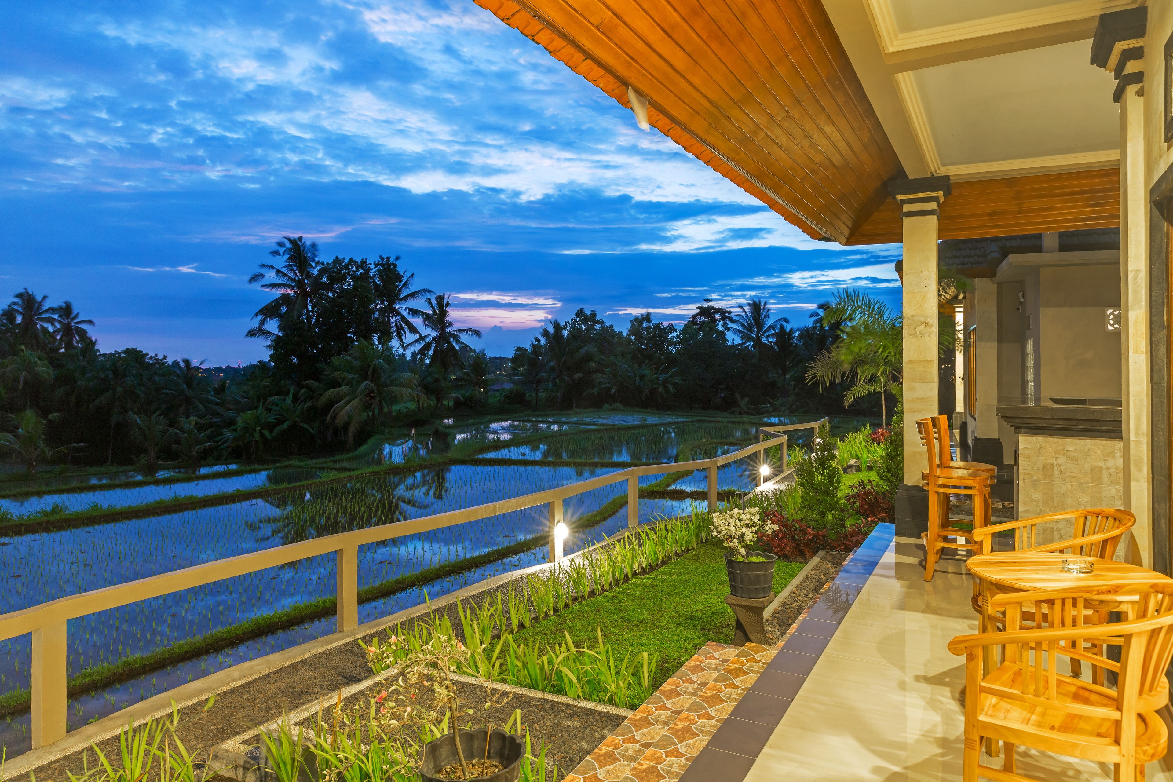 A terrace with a view of rice paddies, wooden chairs, and a railing.