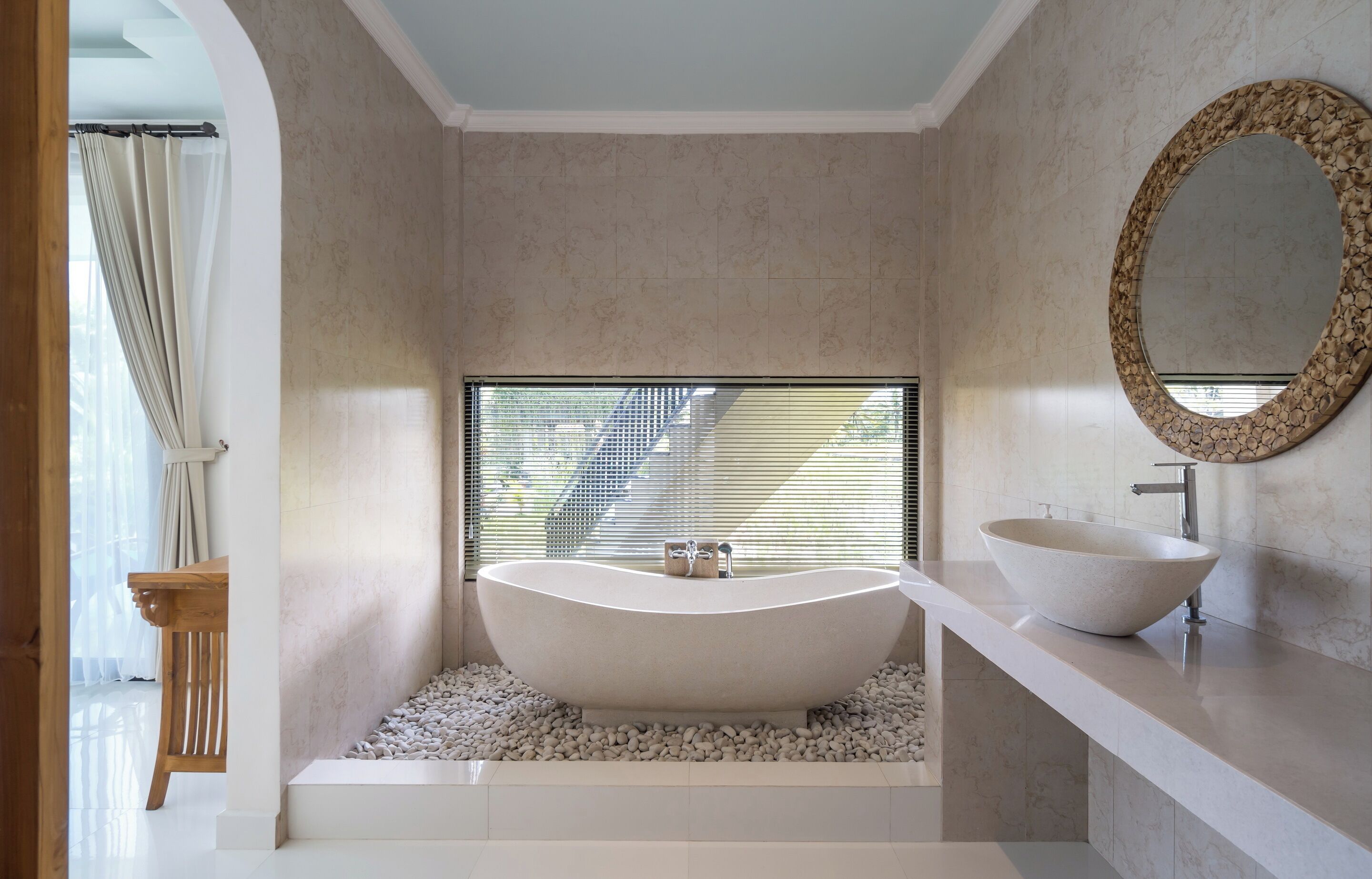 Ein modernes Badezimmer mit einer freistehenden Badewanne, einem großen Spiegel und einem Fenster mit Jalousien.